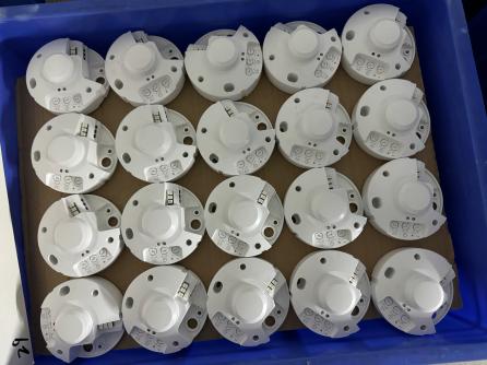 Backs of round sensor units arranged in a blue factory bin